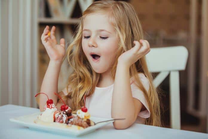 Happy surprised little girl serving ice cream sundae in your coffee .The child sits at a table in a cafe and enjoys. Dia da Criança